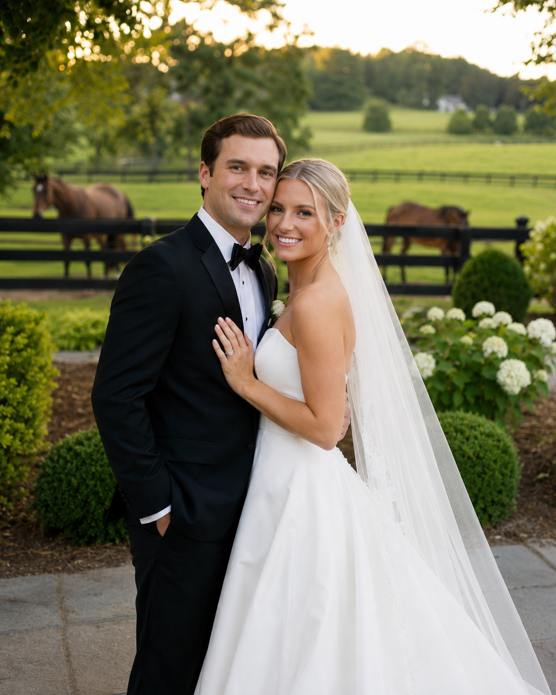 A smiling bride and groom pose together at an outdoor wedding venue with horses and lush greenery in the background.