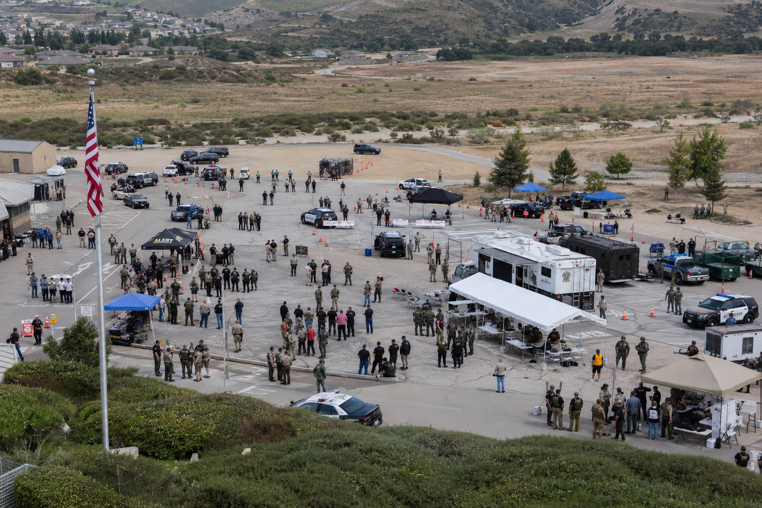 Aerial view of large military or law enforcement gathering with vehicles in desert valley location.
