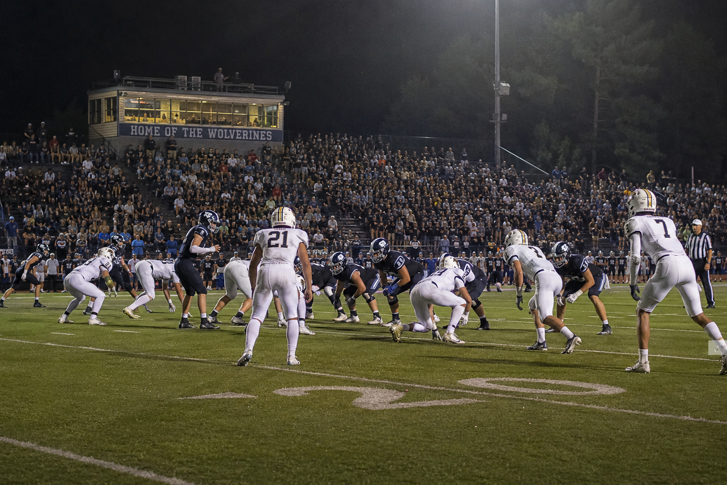 Friday night high school football game under bright stadium lights with packed crowd in stands.