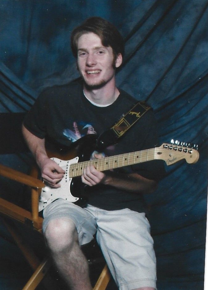 A guitarist in white shorts performs a sequence of poses while playing an electric guitar in a dark room.
