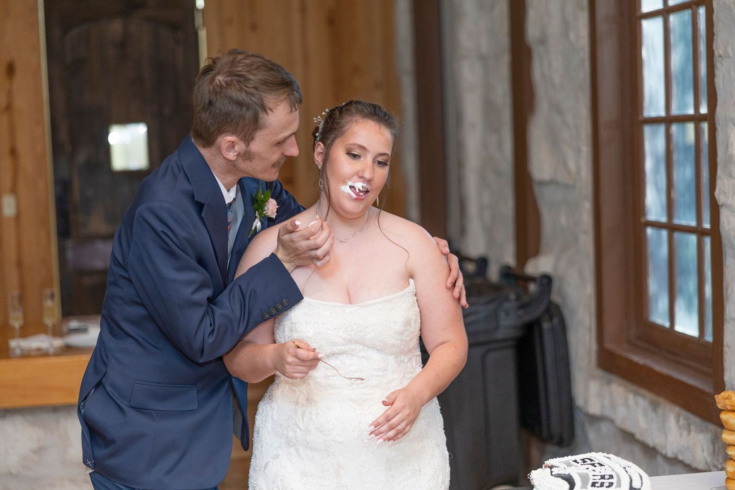 A couple shares an intimate moment during their wedding celebration in a rustic venue with stone walls and windows.