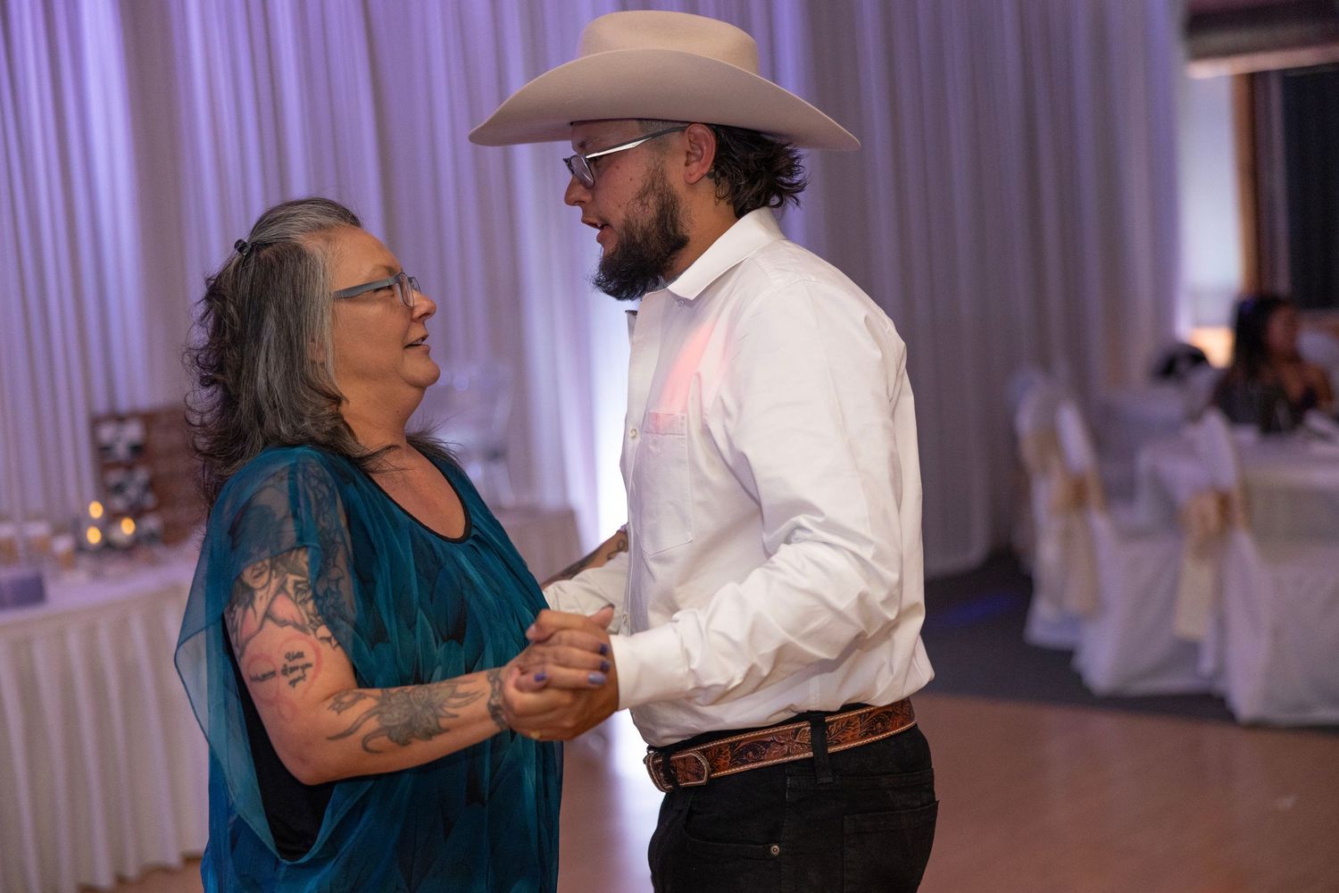 A couple dancing together in a reception hall with white curtained walls and soft lighting in the background.