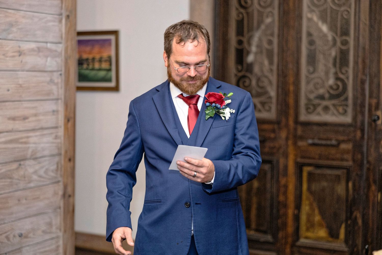 A person in a navy blue suit and red tie reads from a paper while standing in an ornate room with wooden walls.