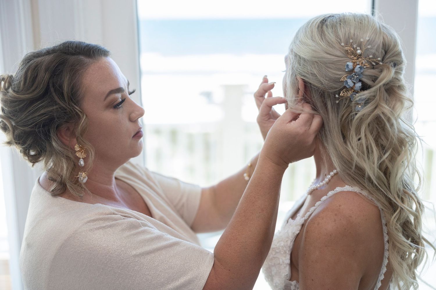 A row of bridesmaids in light colored dresses getting their hair styled at a wedding preparation.