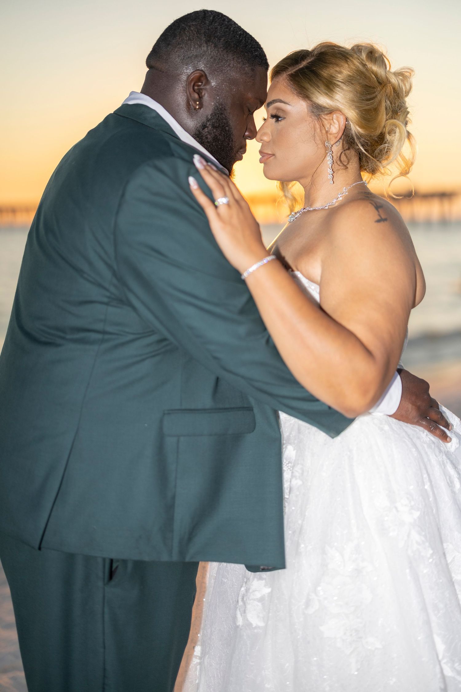 Romantic wedding couple embraces on a beach at sunset with the groom in a dark suit and bride in white dress.