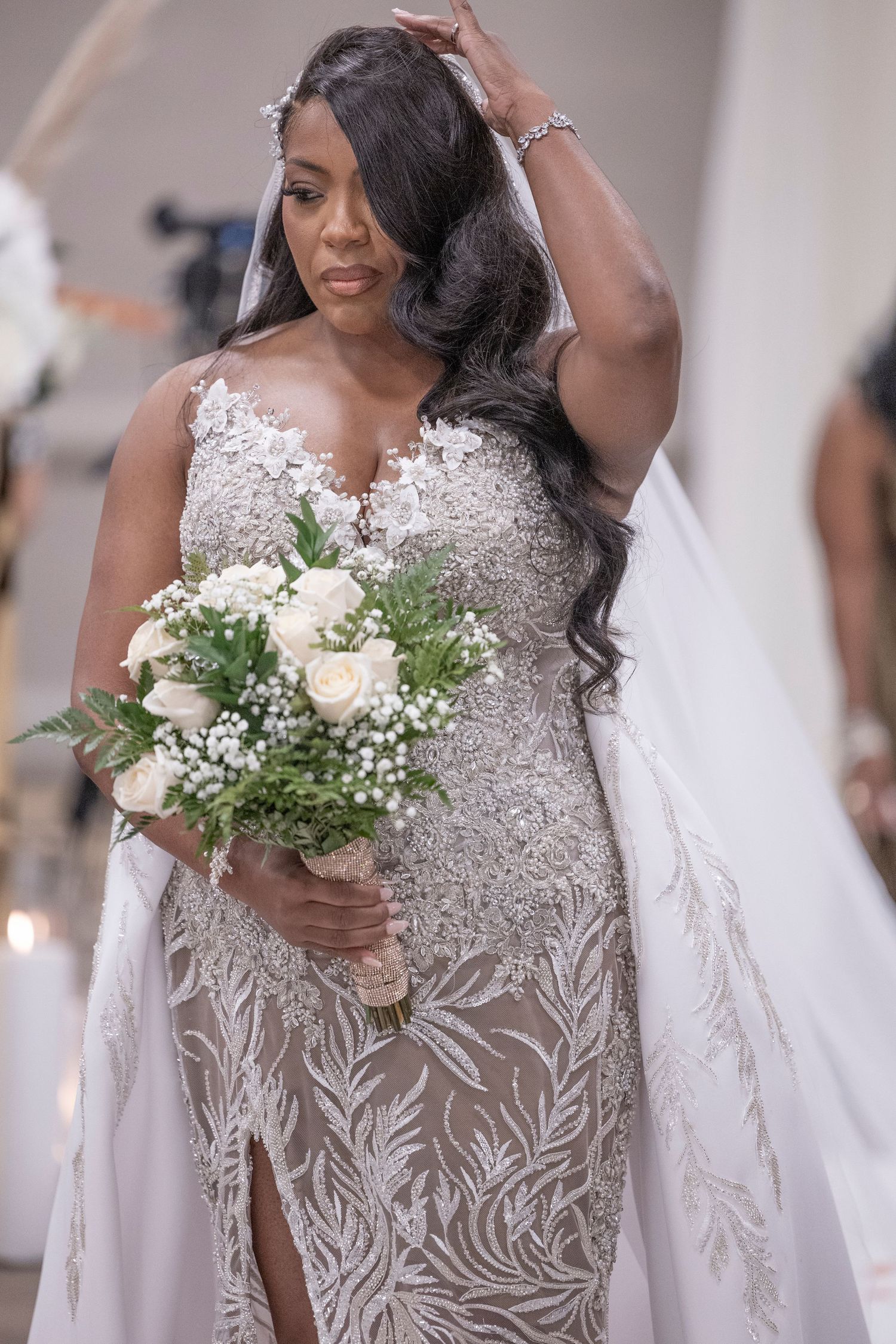 A wedding bouquet of white roses and baby's breath complements an elegant beaded lace gown.