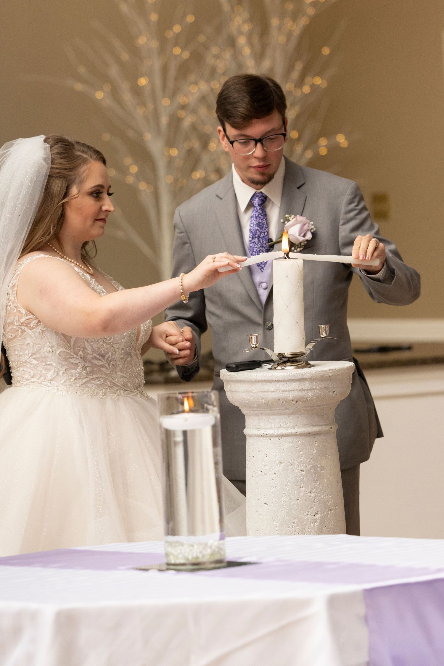 Wedding couple performs unity ceremony at elegant reception with glowing tree backdrop.