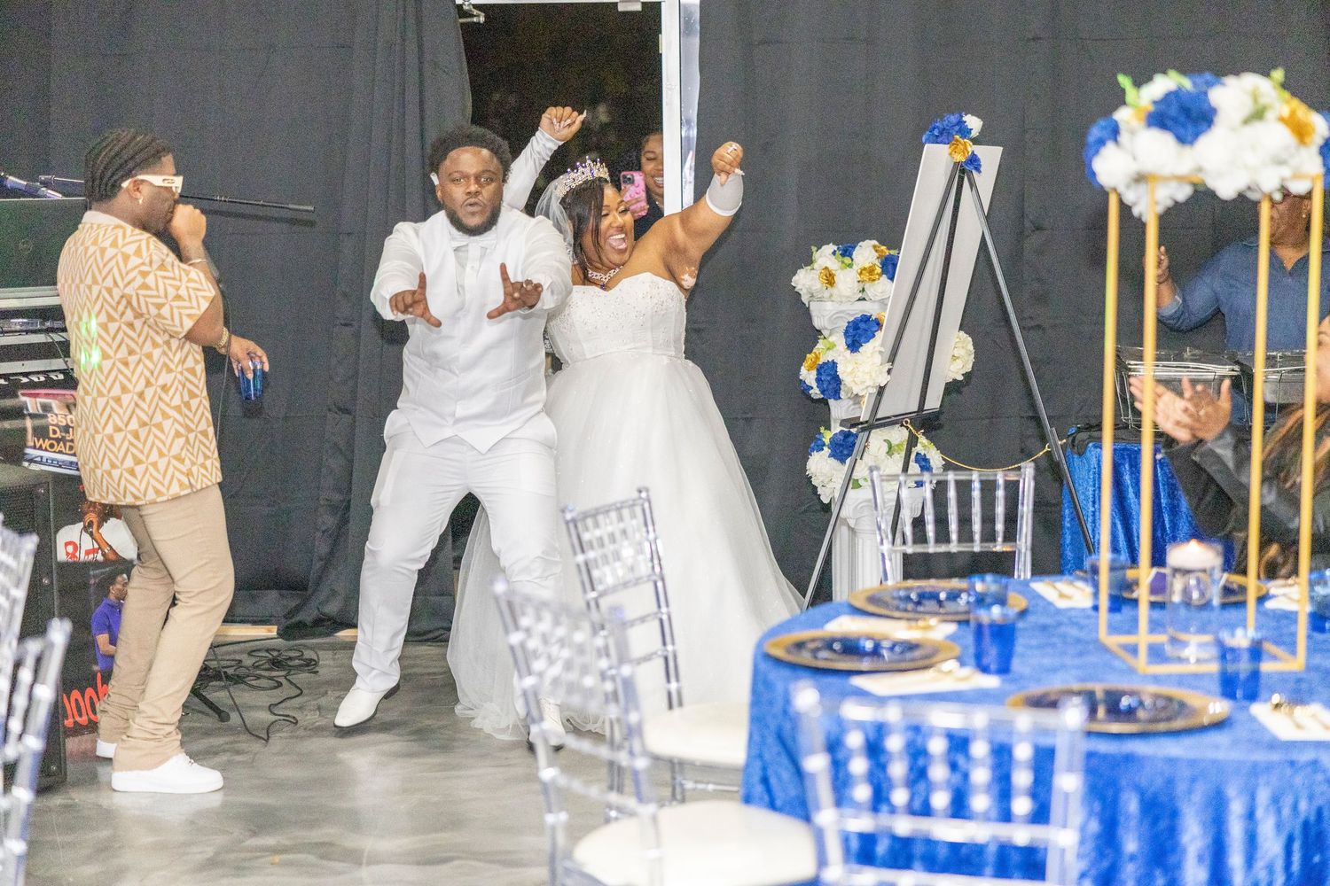 Joyful bride and groom celebrate their wedding reception with guests, featuring elegant blue and gold table decor.