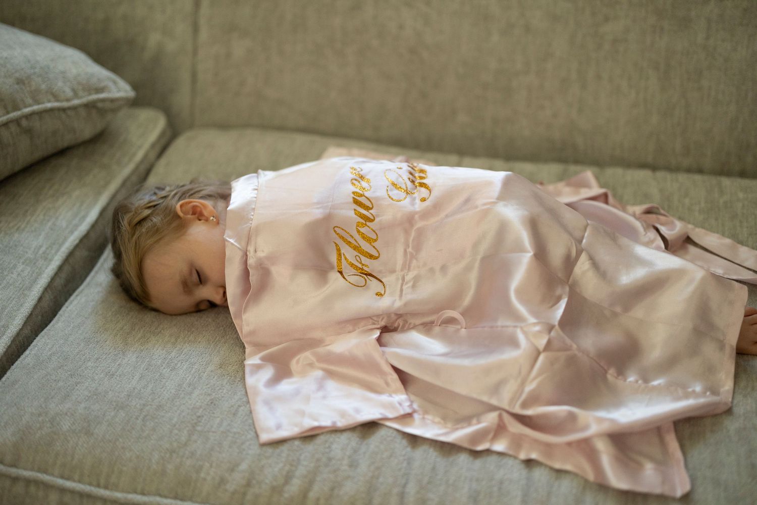 Person sleeping on grey couch wearing pink satin robe with gold text.