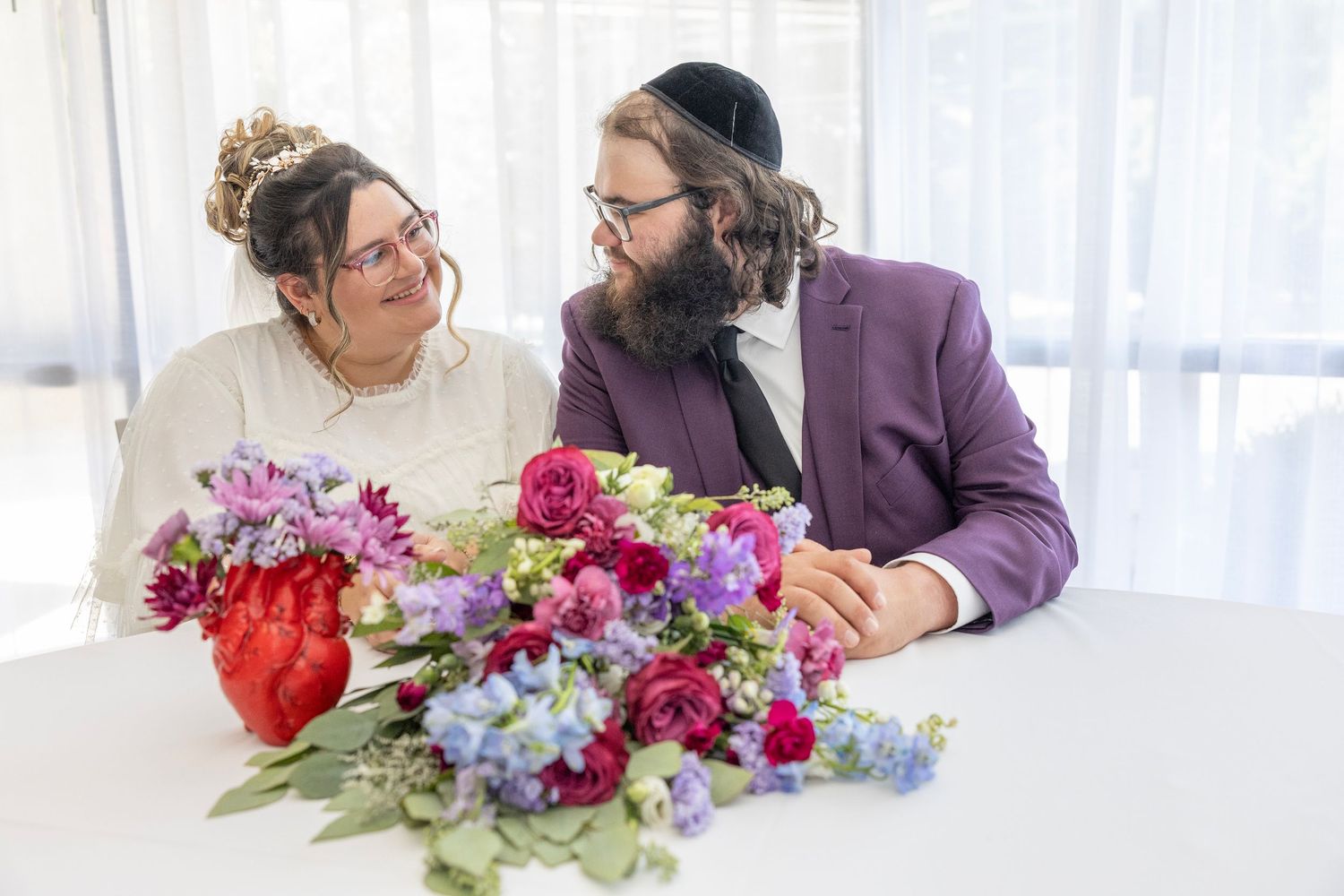 People working together on flower arrangements with colorful blooms including red and purple flowers at a bright table.