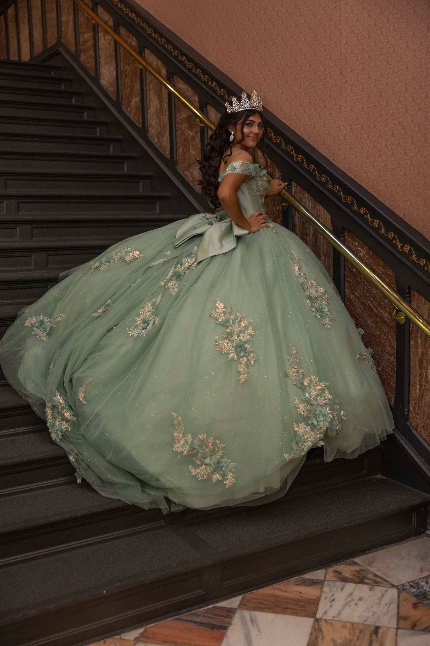 A stunning mint green ball gown with floral appliques adorns a figure posing elegantly on a grand staircase.