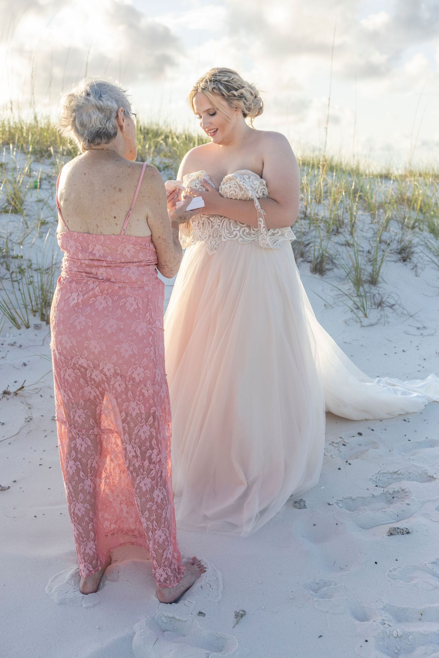 Two people in formal dresses walking together on a sandy beach during sunset, creating a romantic atmosphere.