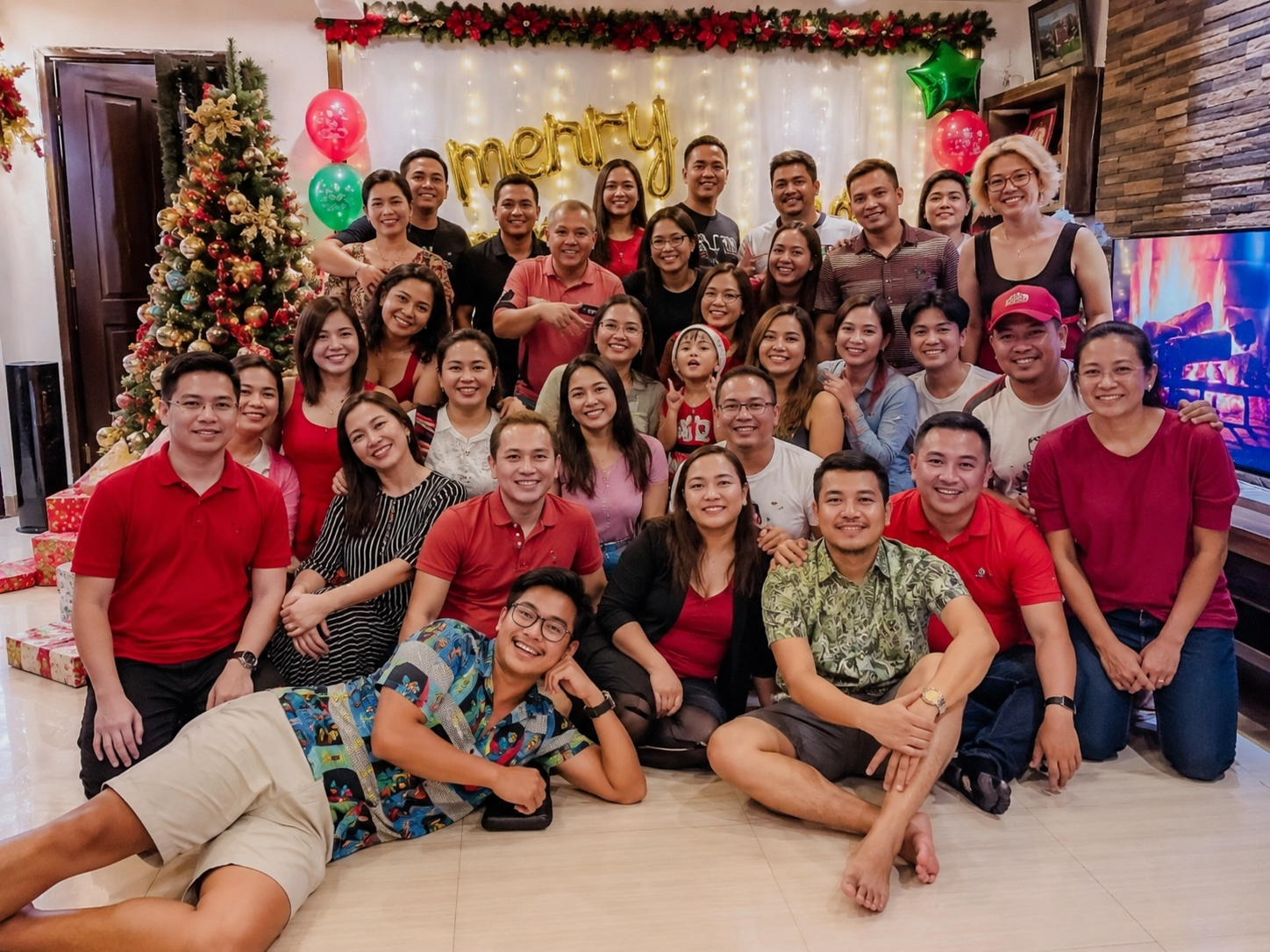 Large group of smiling people pose together at a Christmas celebration with decorated tree.