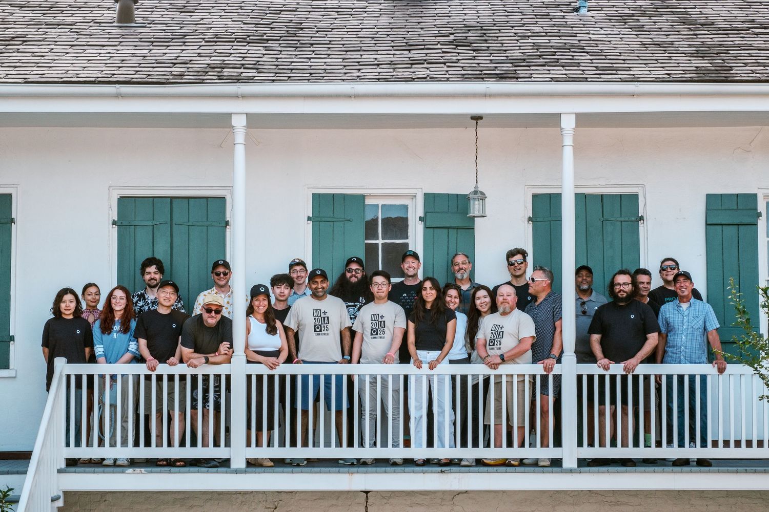 Large group of people gathered on a white porch with turquoise shutters.