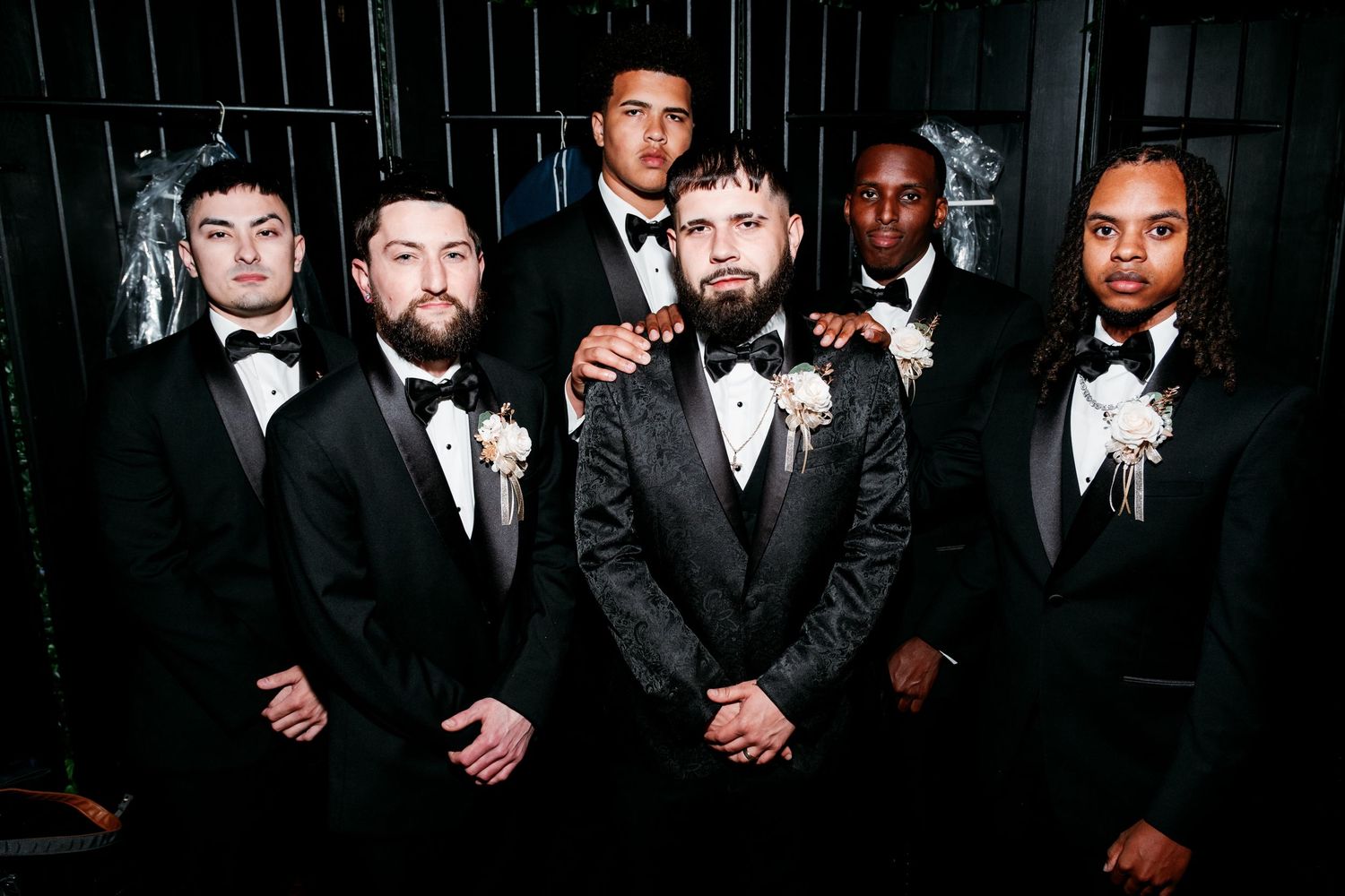 Groomsmen in formal black suits and ties pose together at a wedding celebration.