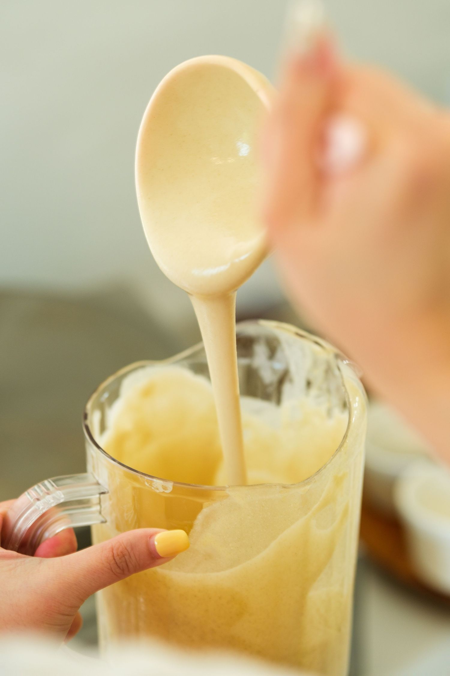 Creamy beige liquid being poured into a clear glass mug.