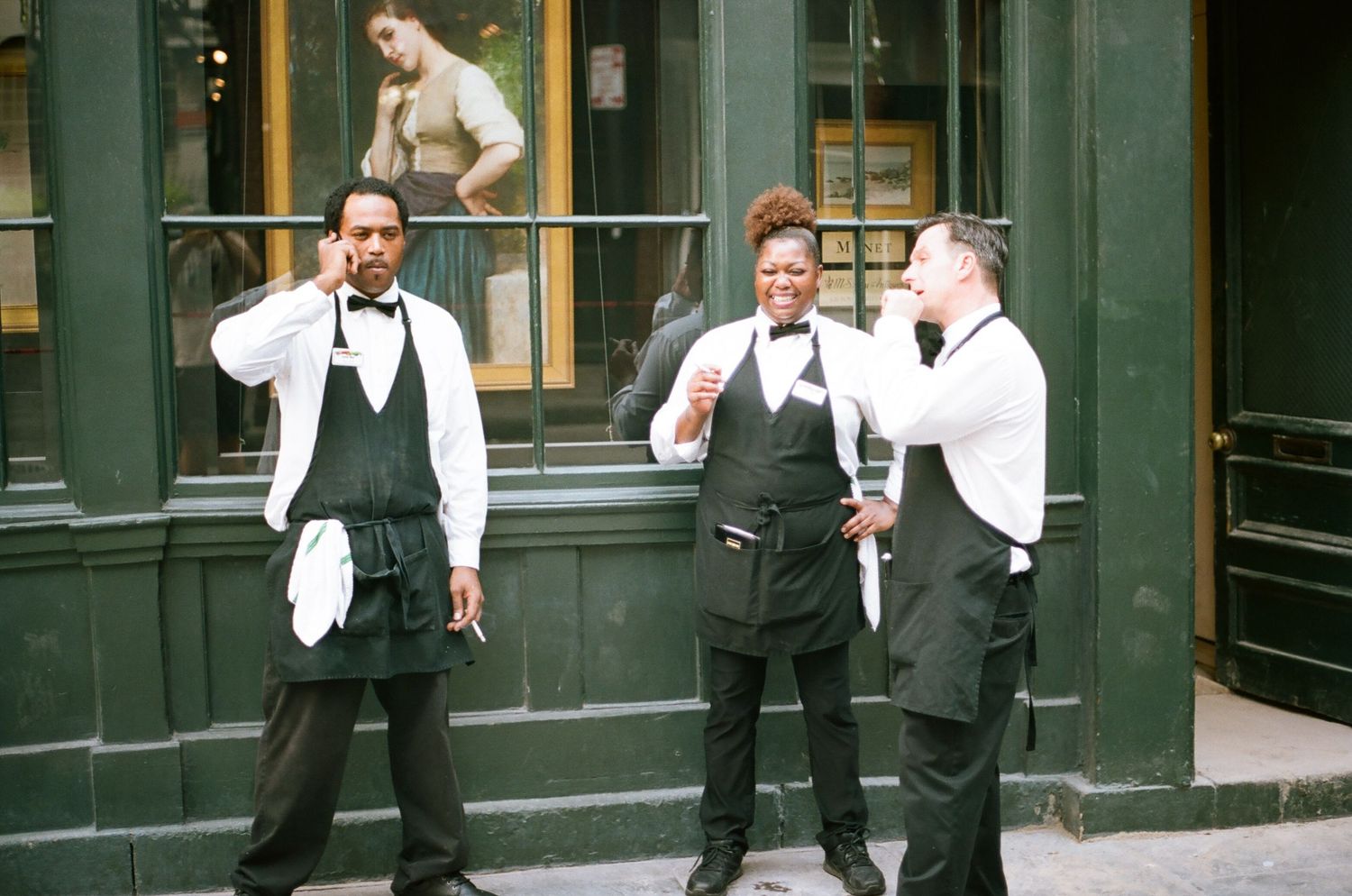Group of waiters in formal attire standing outside a green storefront.