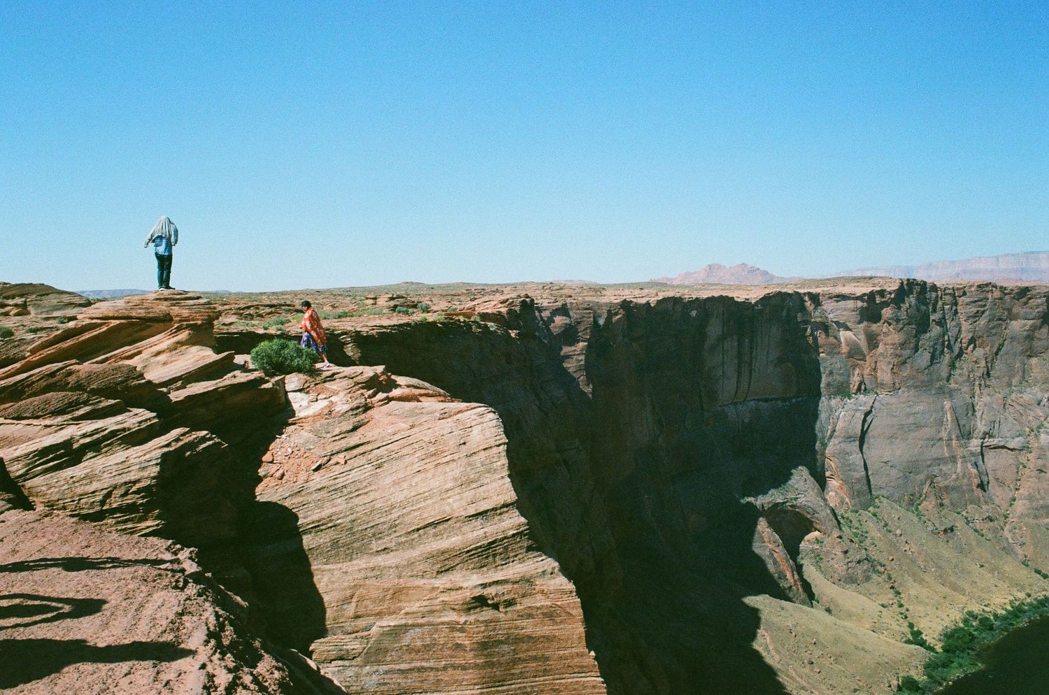 Dramatic panoramic view of red rock cliffs and canyons under clear blue skies in a desert landscape.