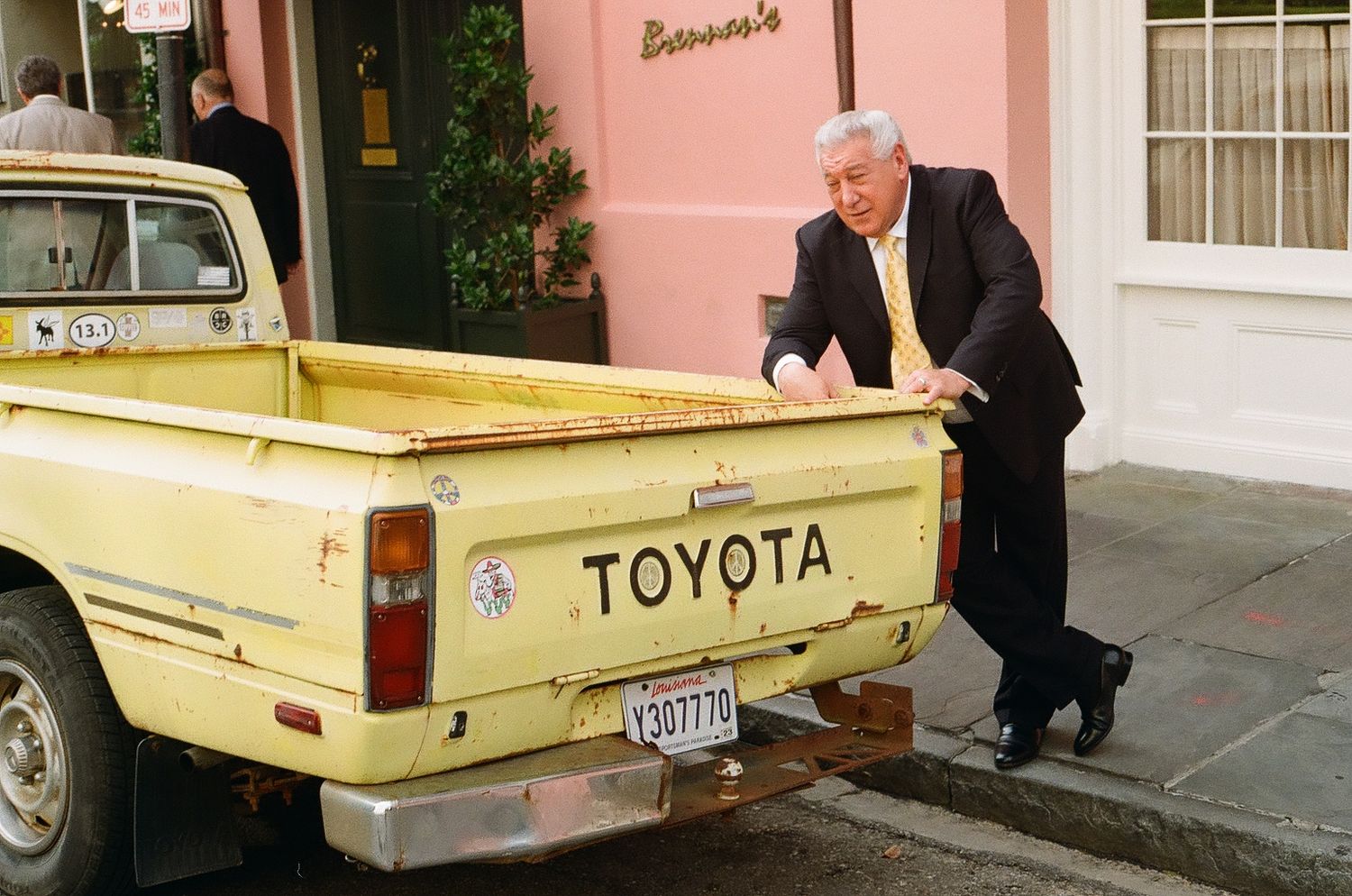 Yellow vintage Toyota pickup truck parked on street near pink building.