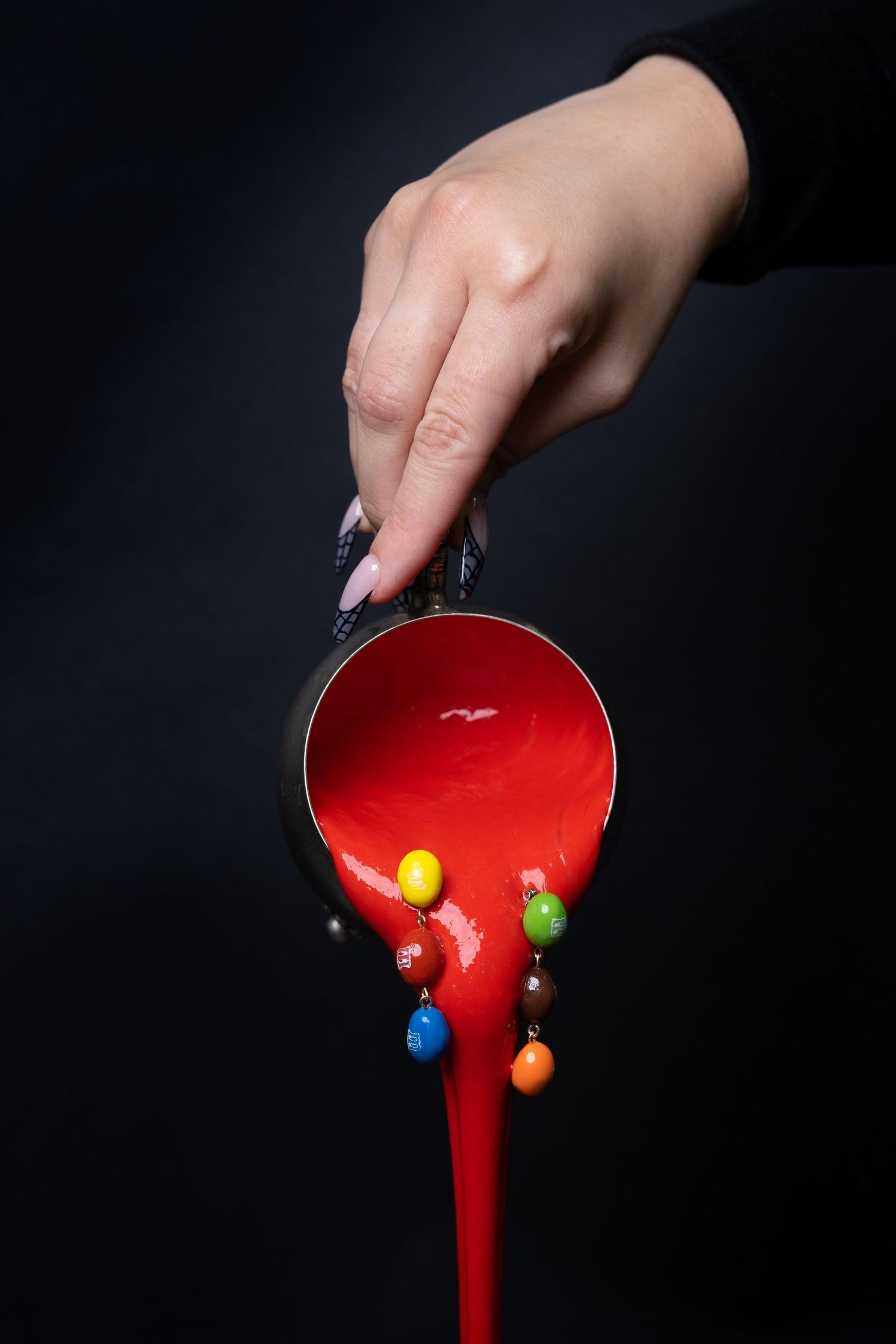 Red liquid dripping with colorful candy decorations against a black background.