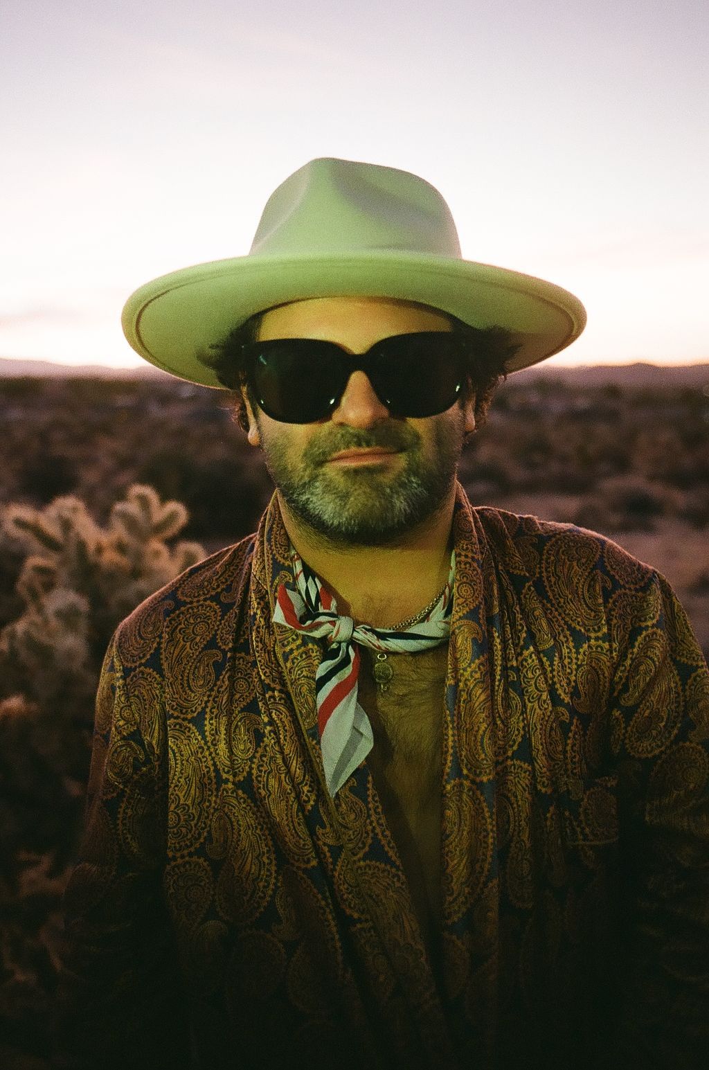 Figure in paisley jacket and green hat photographed at sunset in panoramic style.