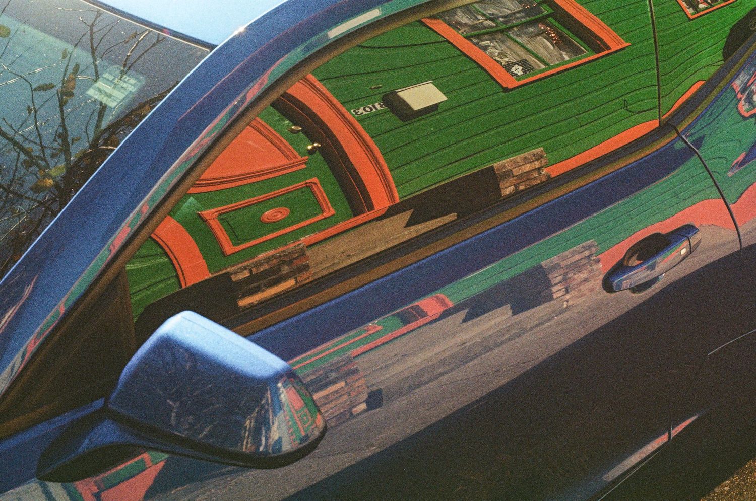 Reflection of vintage architecture in a car's glossy surface showing green and orange details.