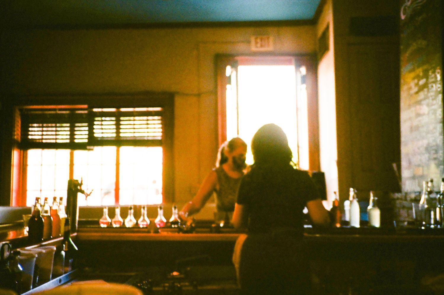 Dark interior bar scene with warm lighting and silhouettes of patrons at tables.