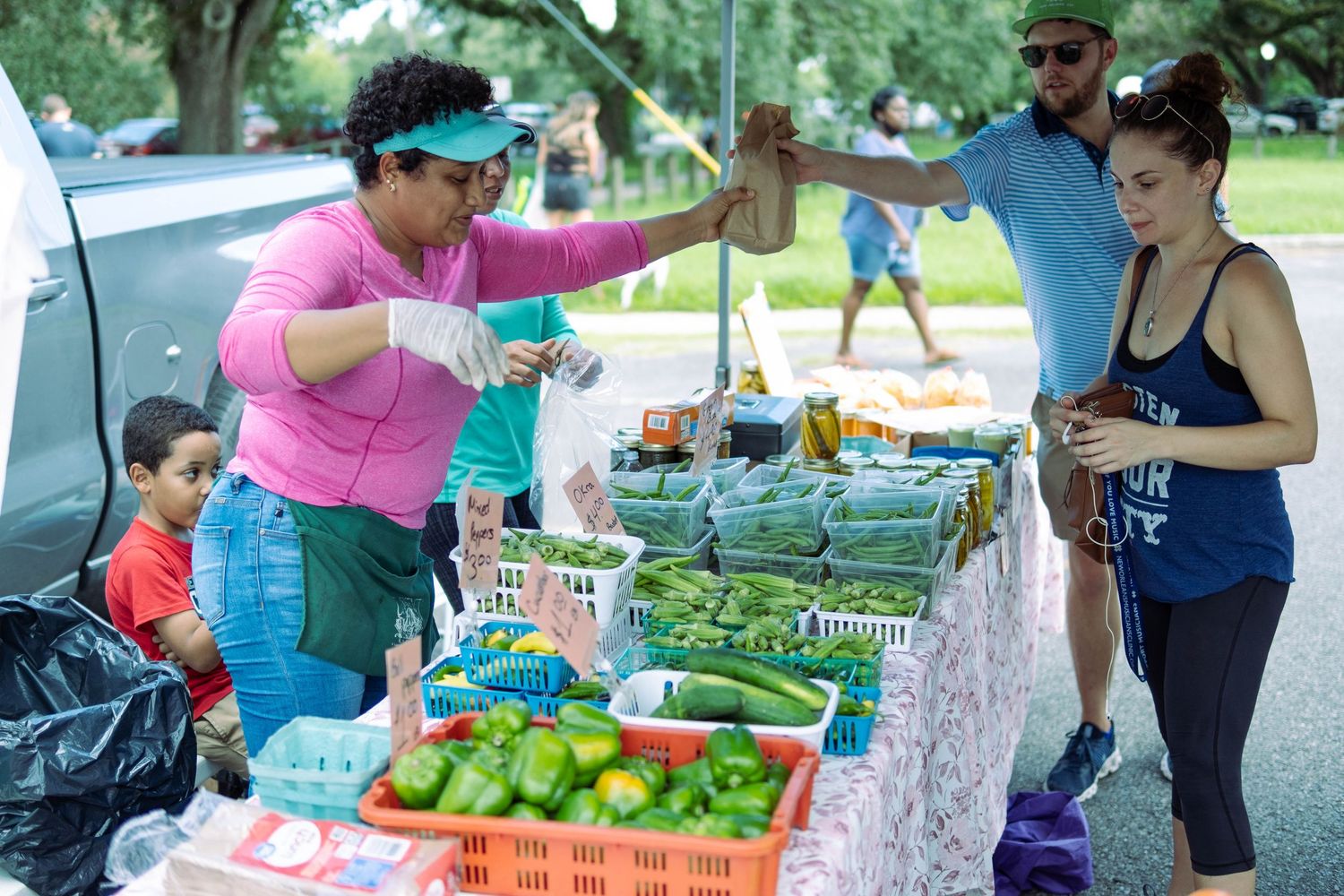 Customers browsing fresh produce and vegetables at an outdoor farmers market.