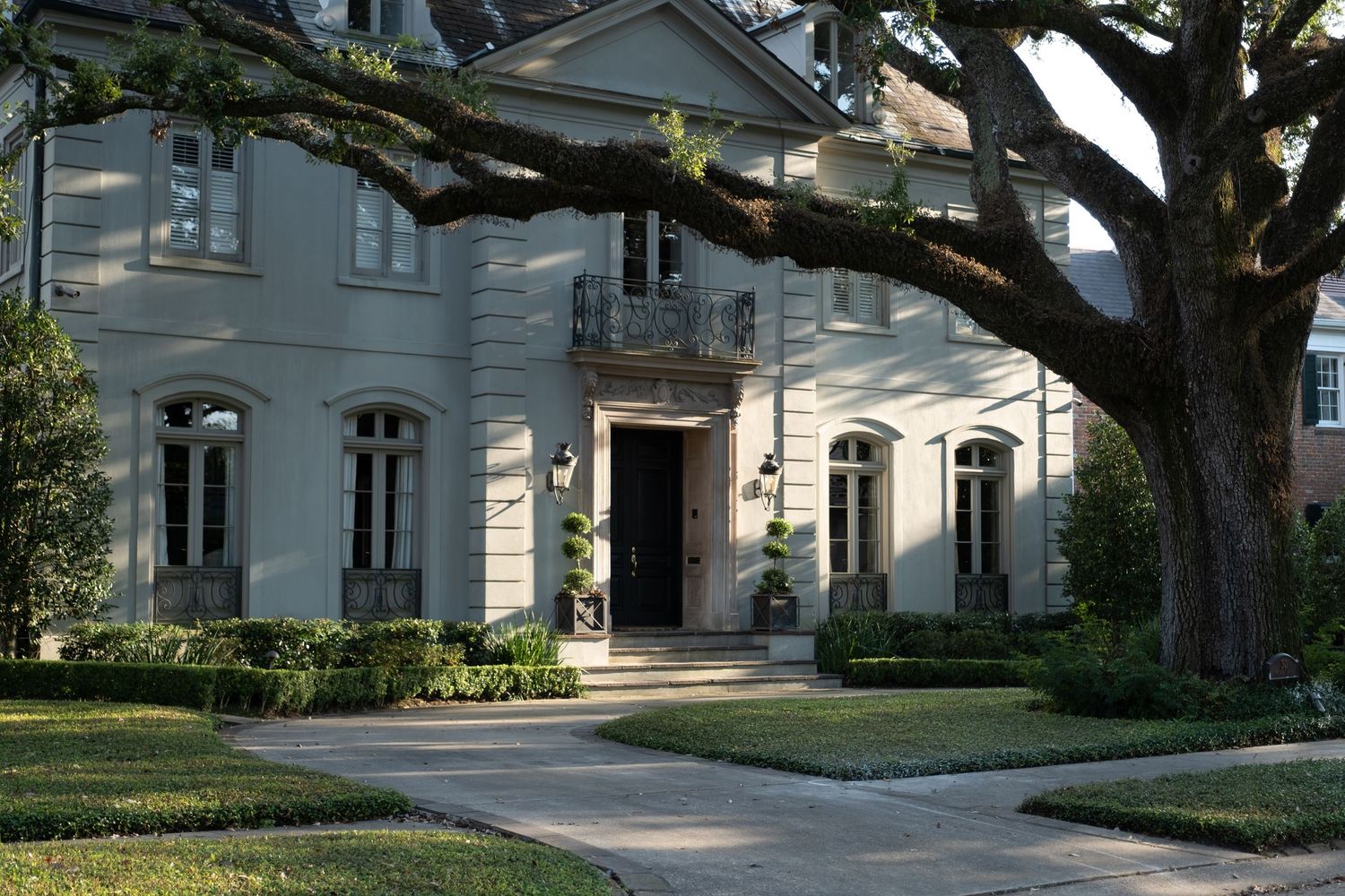 Stately home exterior with large oak tree casting shadows on the driveway.
