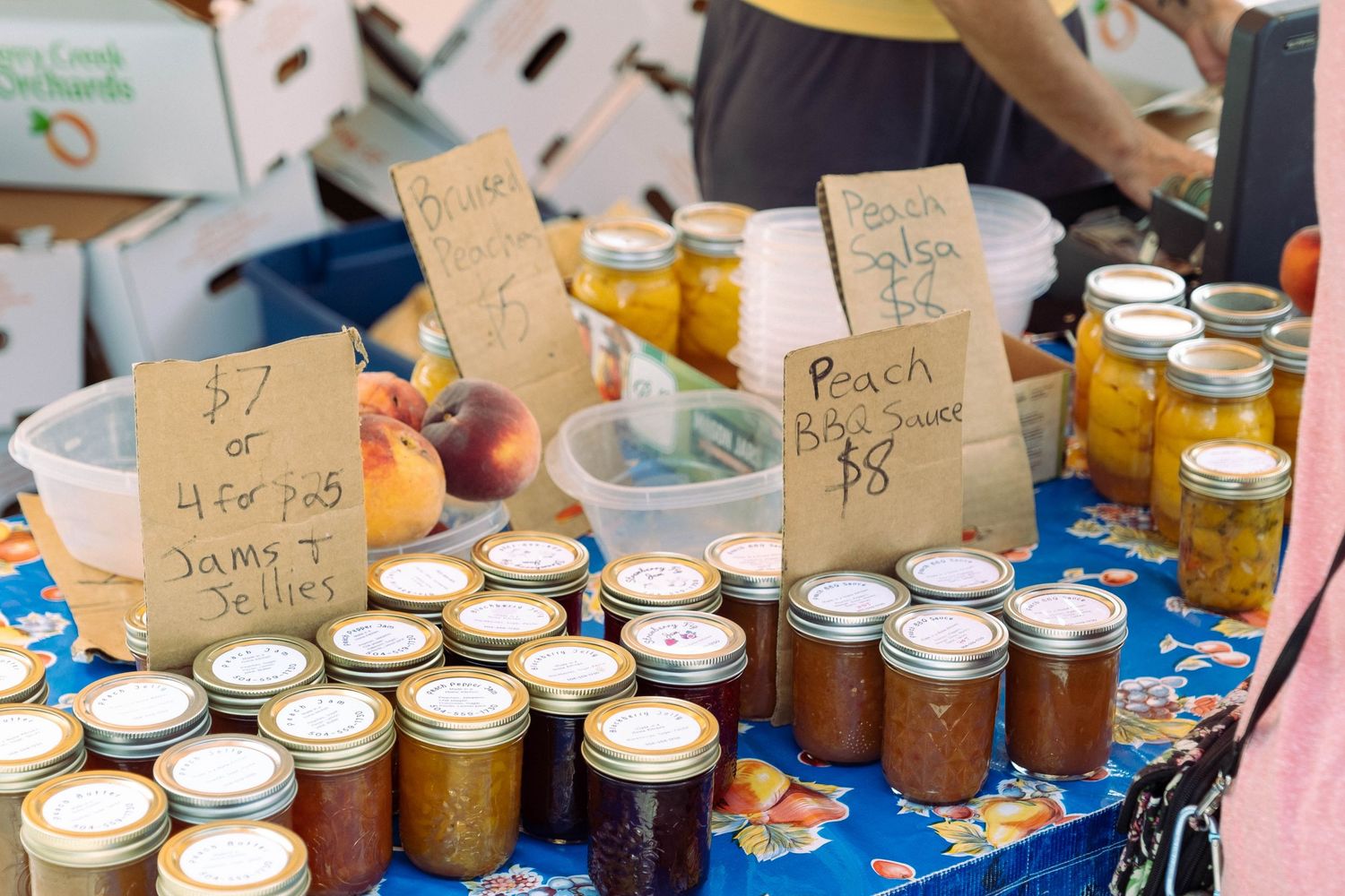 Rows of homemade preserves and canned goods displayed at a farmers market with handwritten labels.
