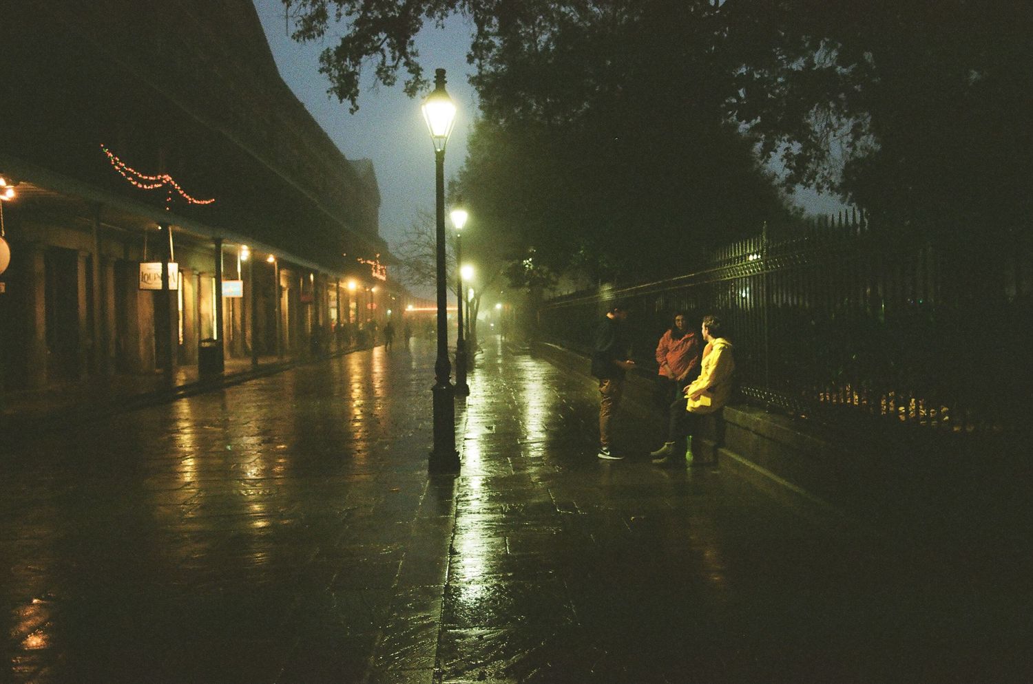 Atmospheric nighttime view of a historic street with glowing lampposts casting reflections on wet pavement.
