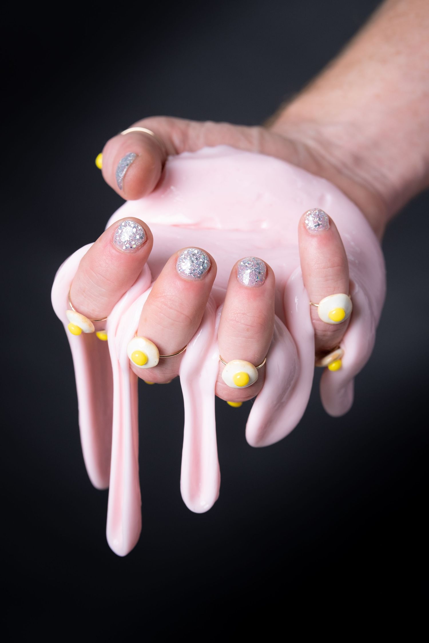 Hands with yellow and silver glitter nail polish displayed against dark background.