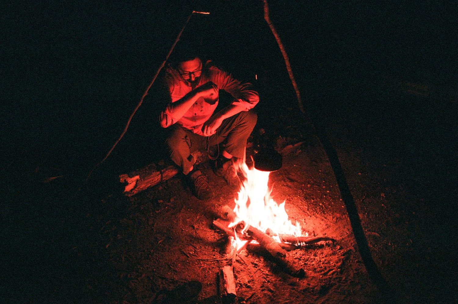 Campfire glowing red in the darkness with figures gathered around.