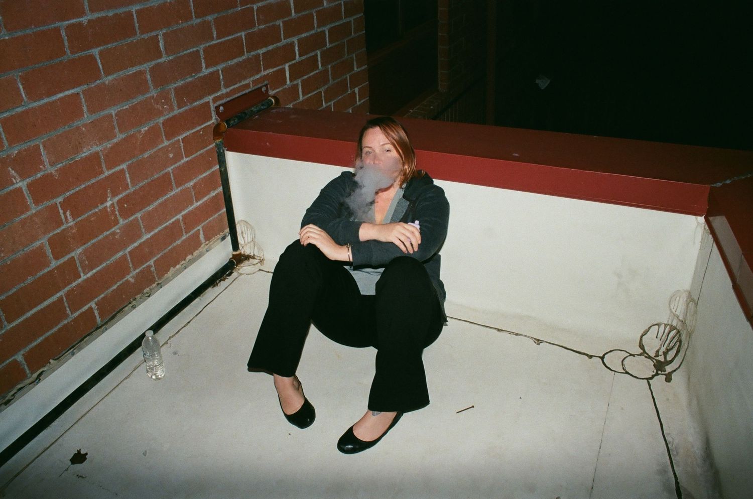 Person sitting against brick wall in dramatic black and white composition.