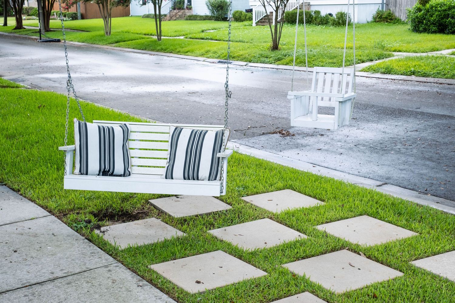 Concrete stepping stones leading through a green lawn in front of residential homes.