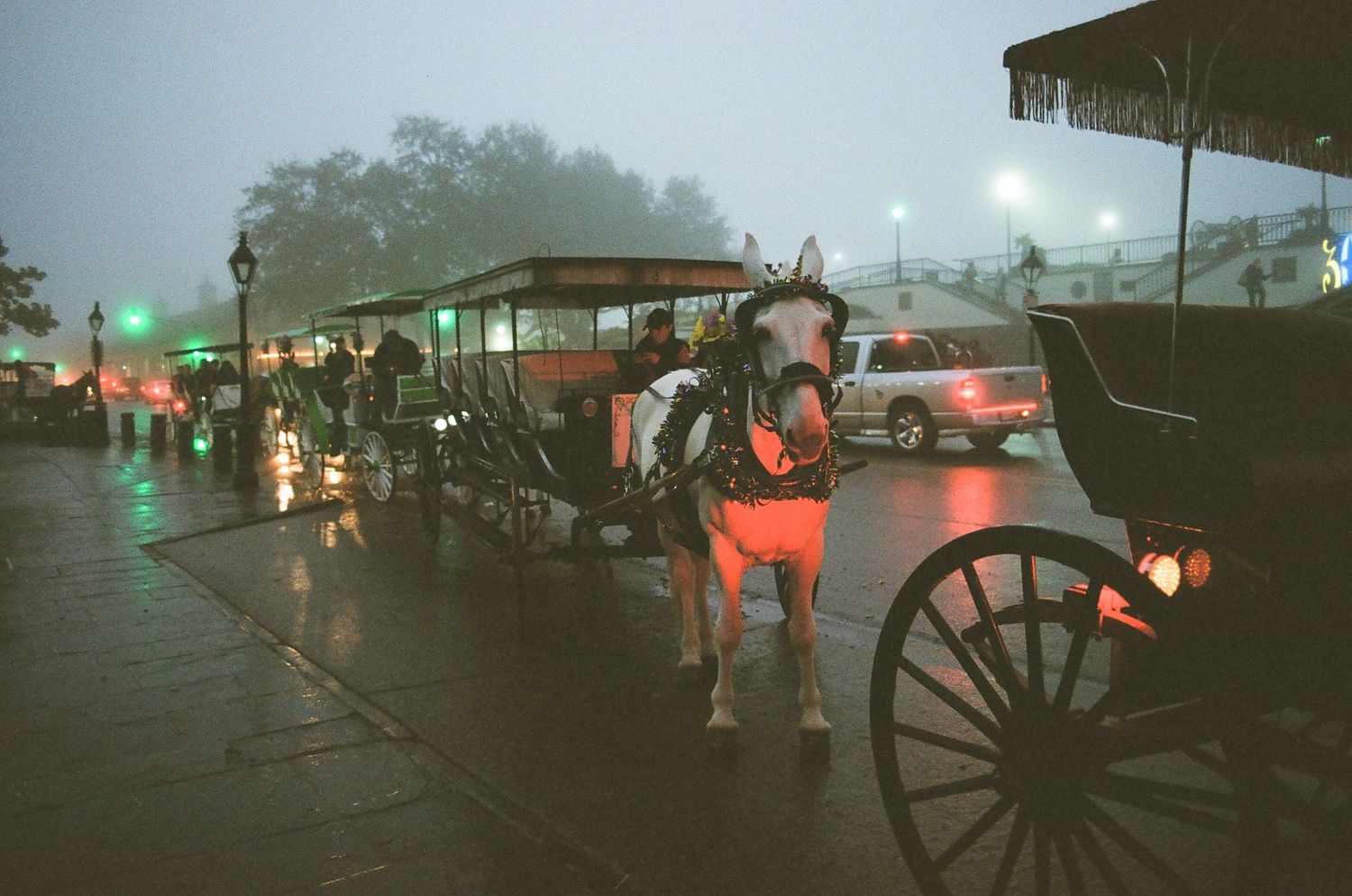 Rainy night scene on a historic street with horse-drawn carriages and glowing lampposts reflecting on wet cobblestones.