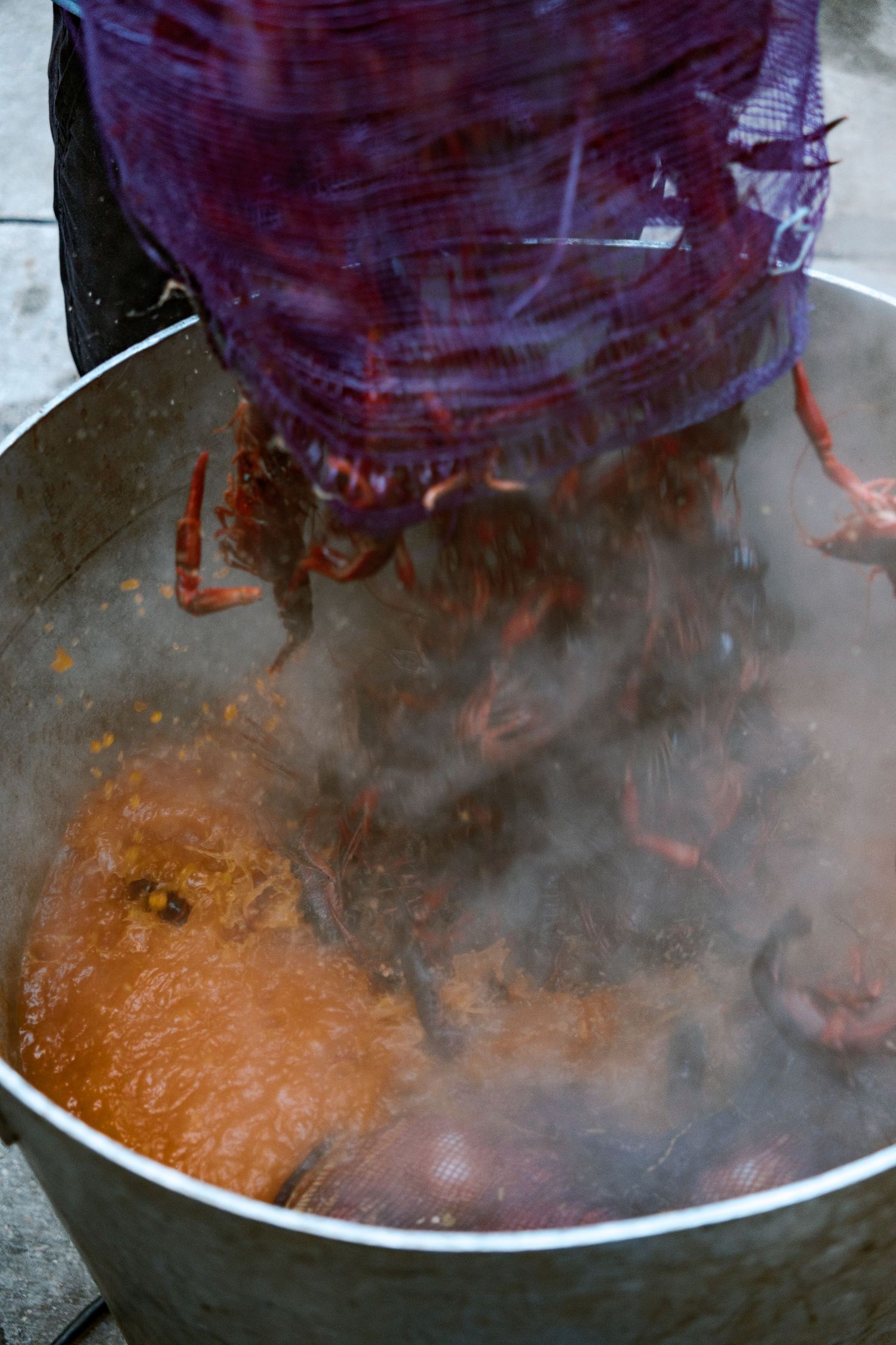 Large pot of steaming red sauce being stirred in commercial kitchen.