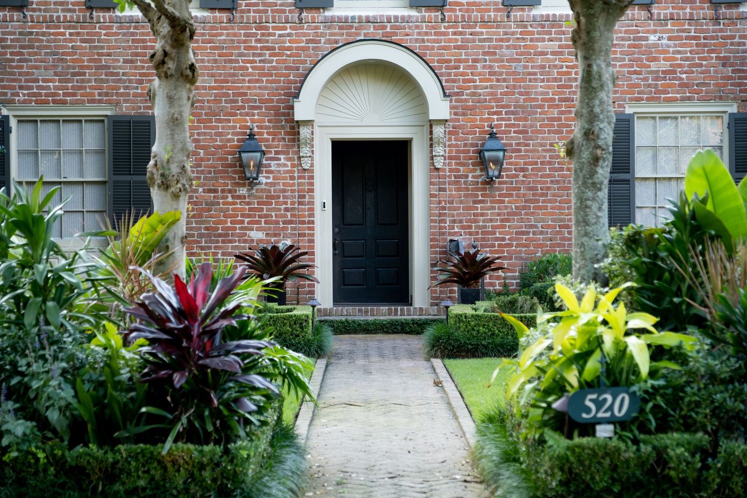 Red brick house entrance with tropical plants and landscaped pathway.