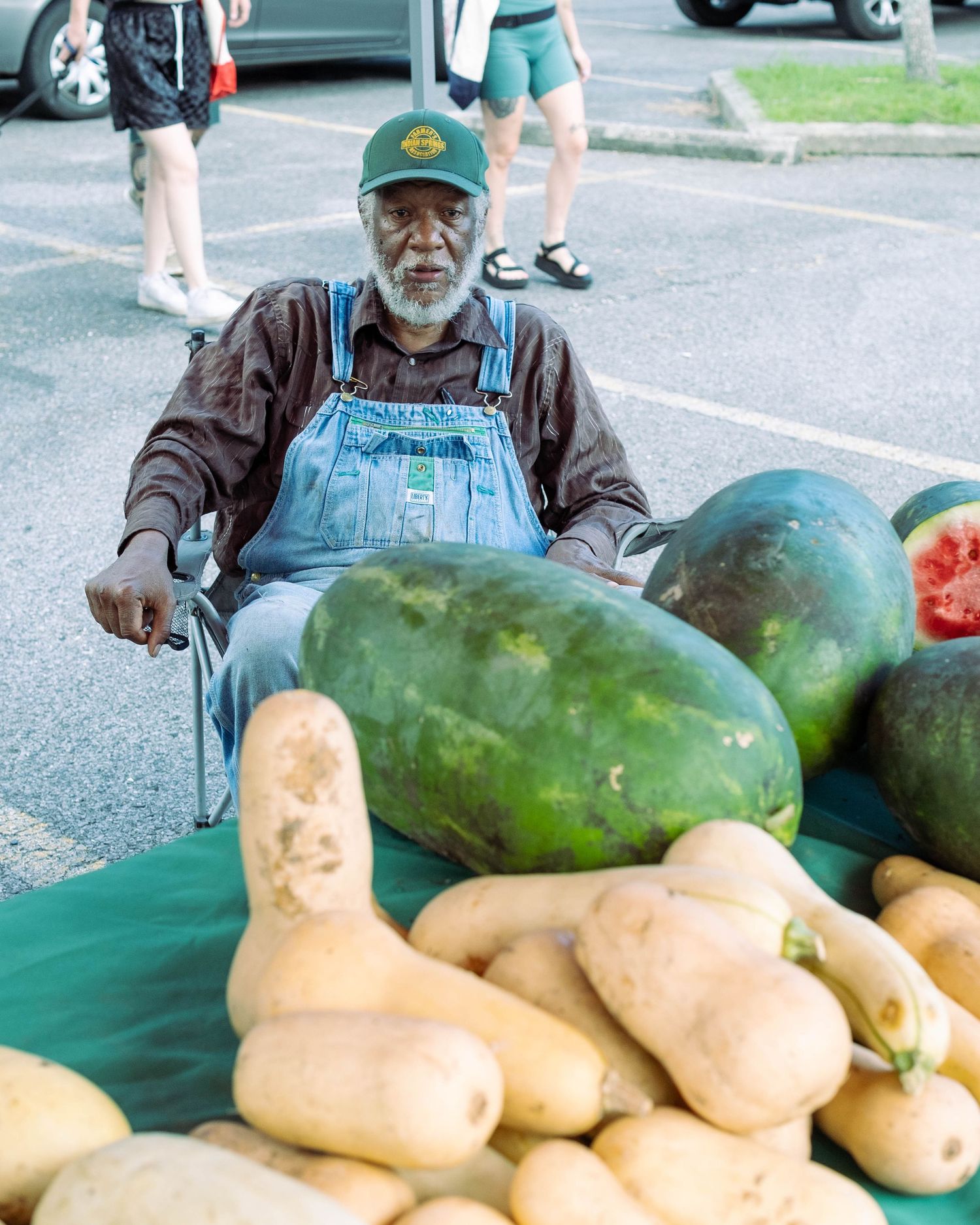 Fresh watermelons and butternut squash displayed on a green tablecloth at an outdoor market.