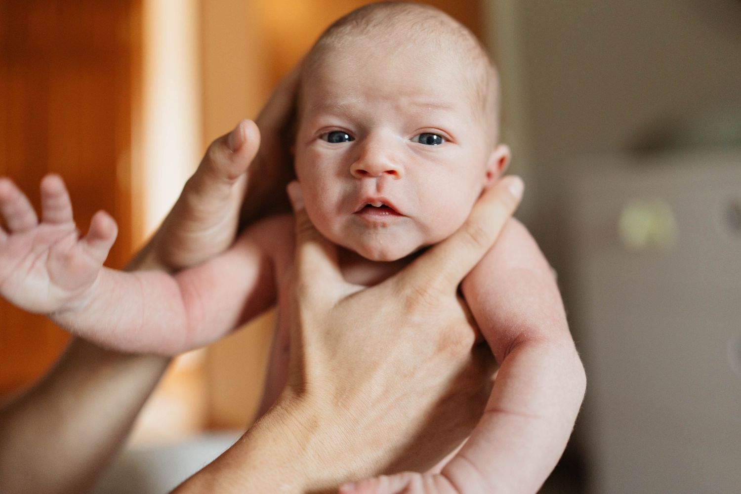 Two hands carefully hold a newborn baby while checking various areas of the infant's body.