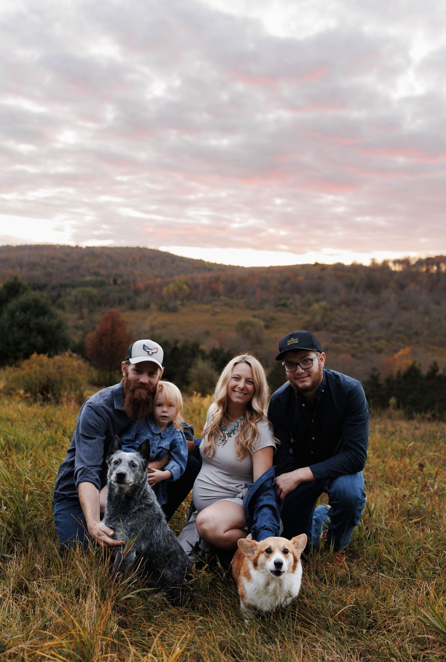 Family and their two dogs sitting together in an autumn field during sunset with mountains in the background.