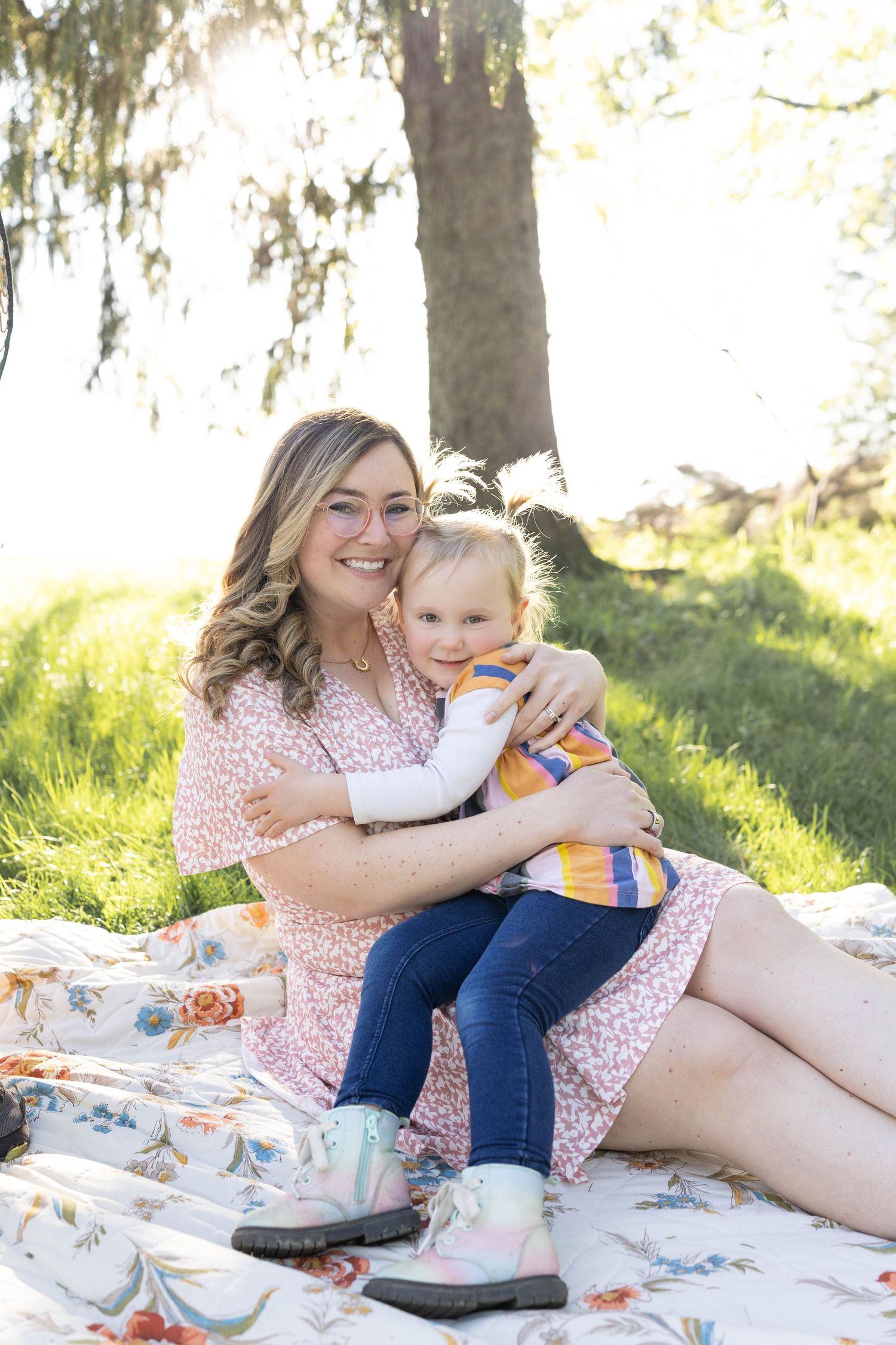 Mother and young child share a tender moment while sitting on a blanket in a sunny park setting during a spring day.