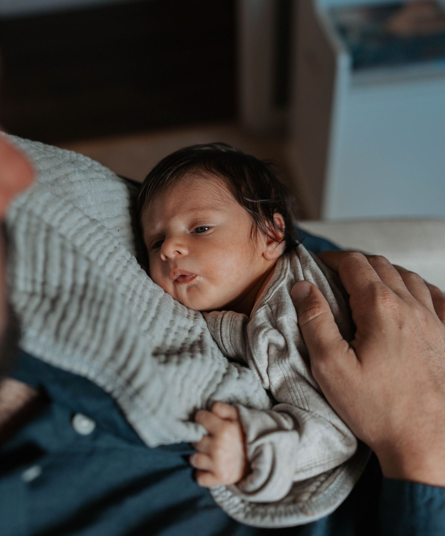 Newborn baby resting peacefully in parent's arms, wearing a soft knit onesie in a cozy home setting.