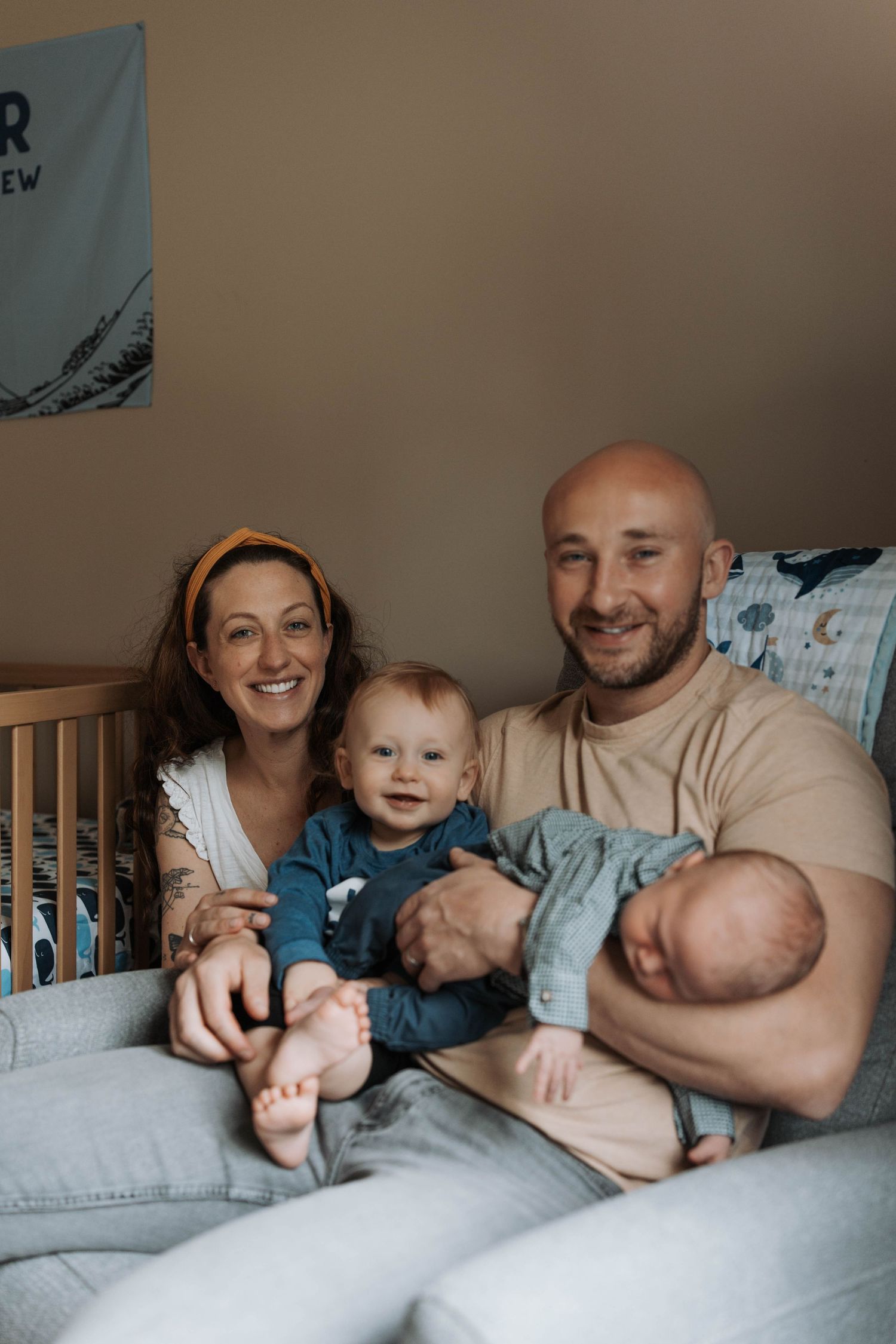 Happy family of four with two young children posing together on a couch in a nursery room.
