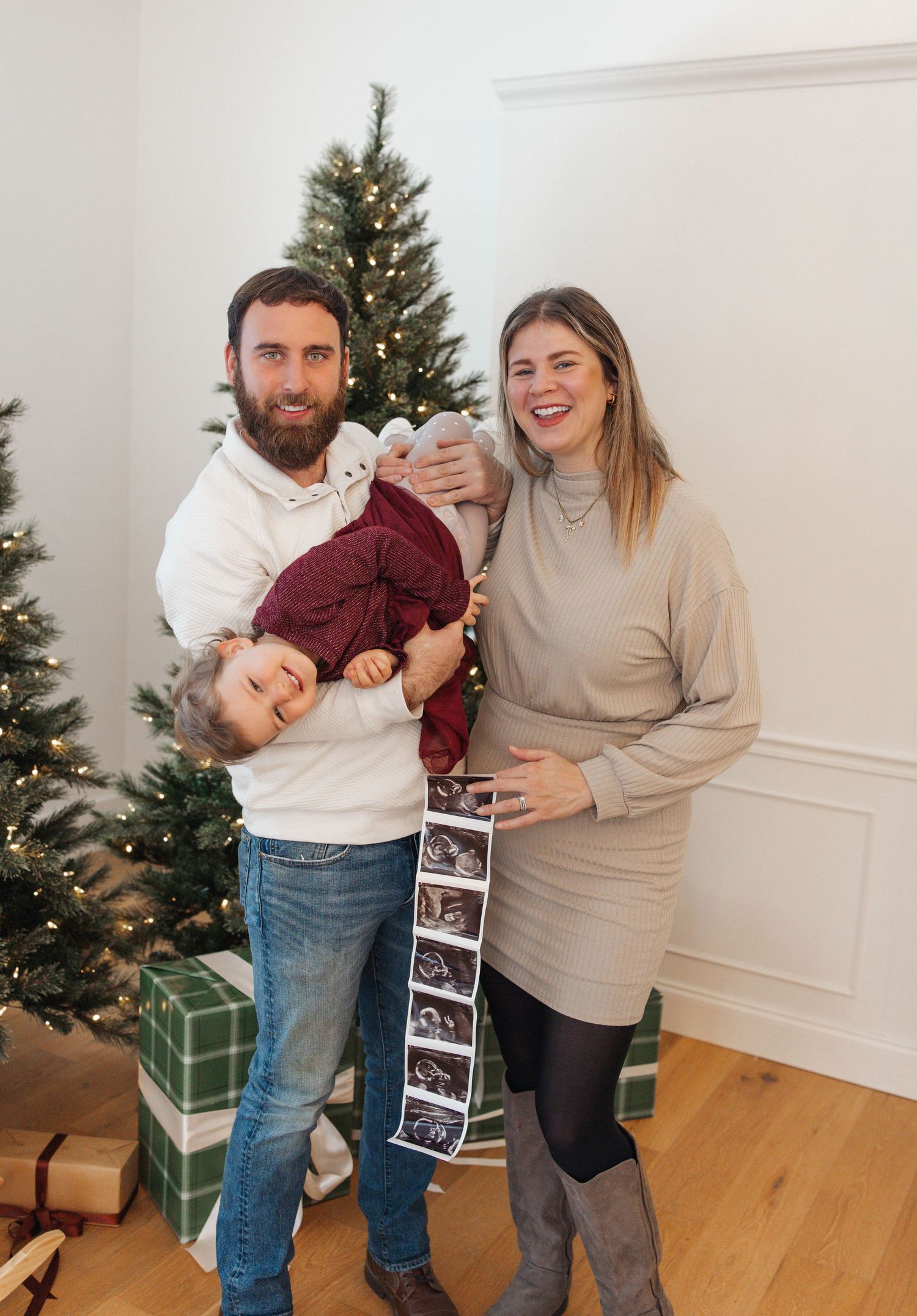 Couple stands by Christmas tree sharing ultrasound photos and embracing in joyful pregnancy announcement series.