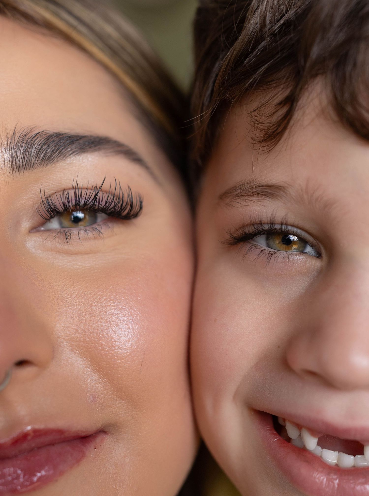 Close-up portrait of a woman with glamorous lashes and a young boy cheek to cheek, both with hazel eyes.