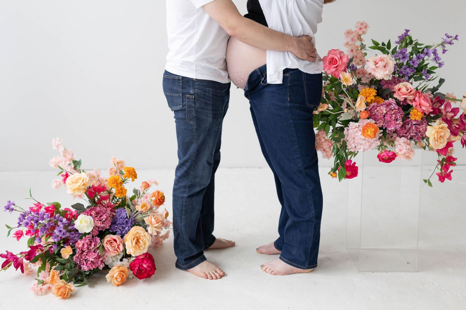 Two people in blue jeans holding colorful floral arrangements with roses, peonies and wildflowers against white background.
