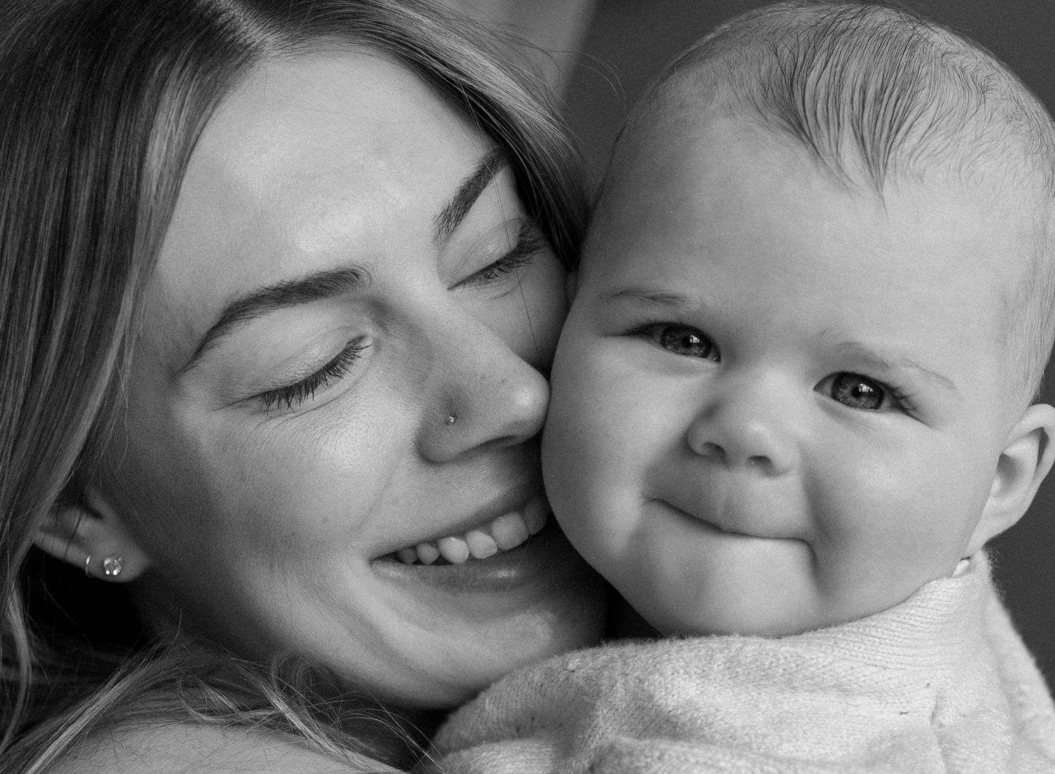 Black and white photo of a smiling young mother cheek to cheek with her happy chubby baby.