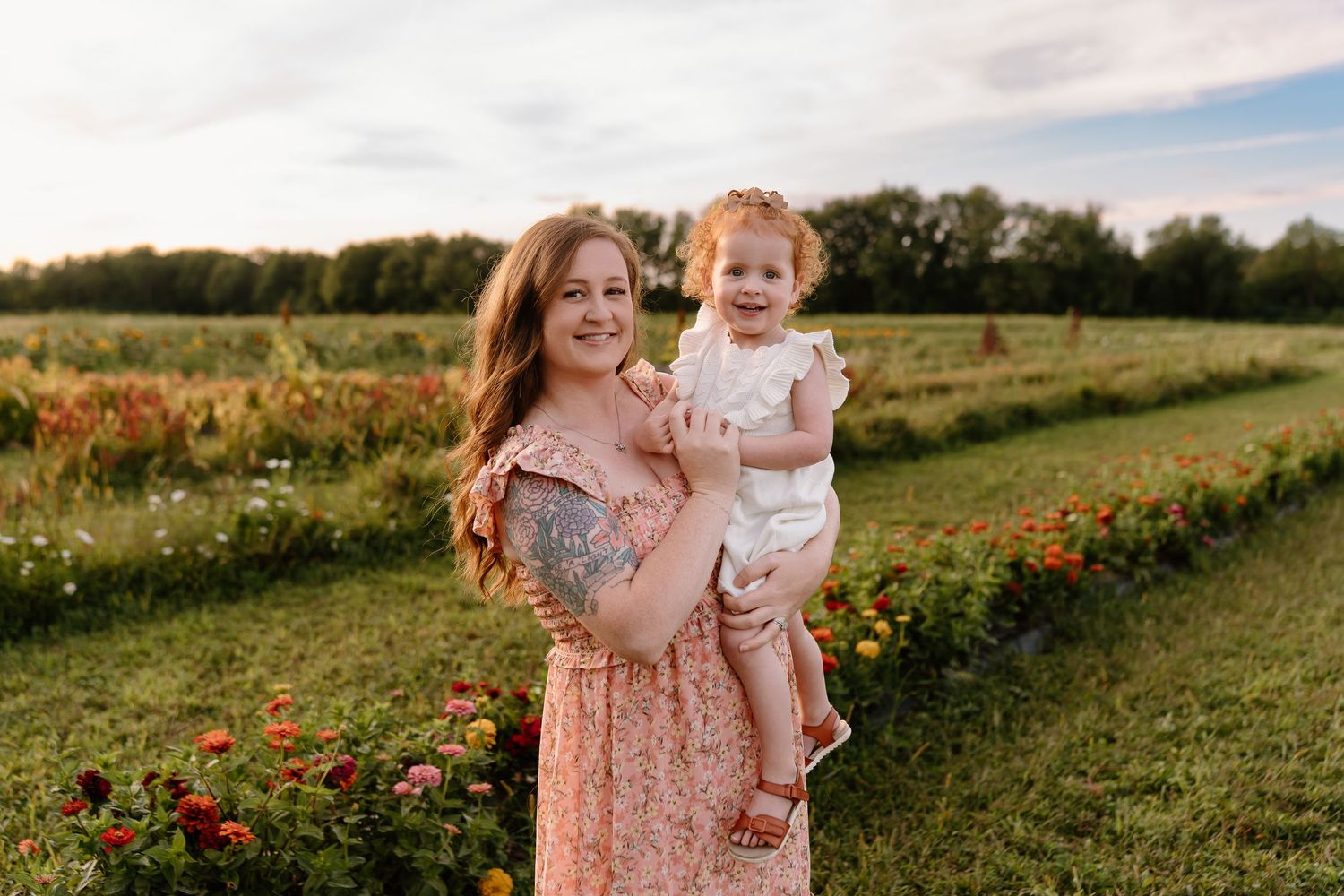 People in floral pink dresses walk through a wildflower meadow at sunset creating a dreamy summer scene.
