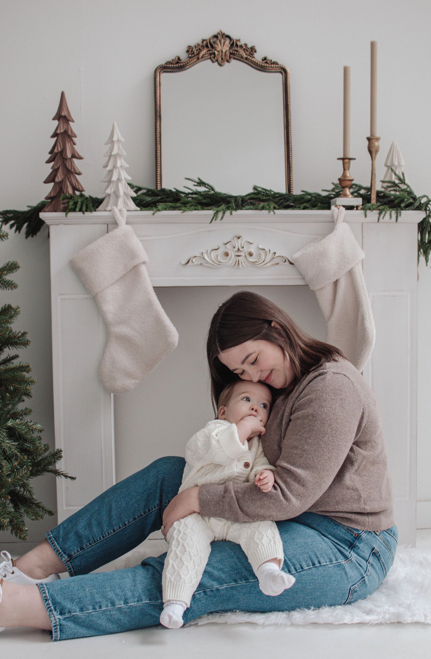 Cozy Christmas scene with fireplace mantel decorated with greenery, stockings, mirror and candles on white mantle.